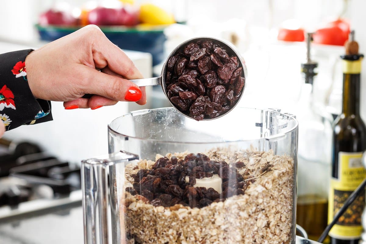 Adding dried fruit to a food processor with toasted oats.