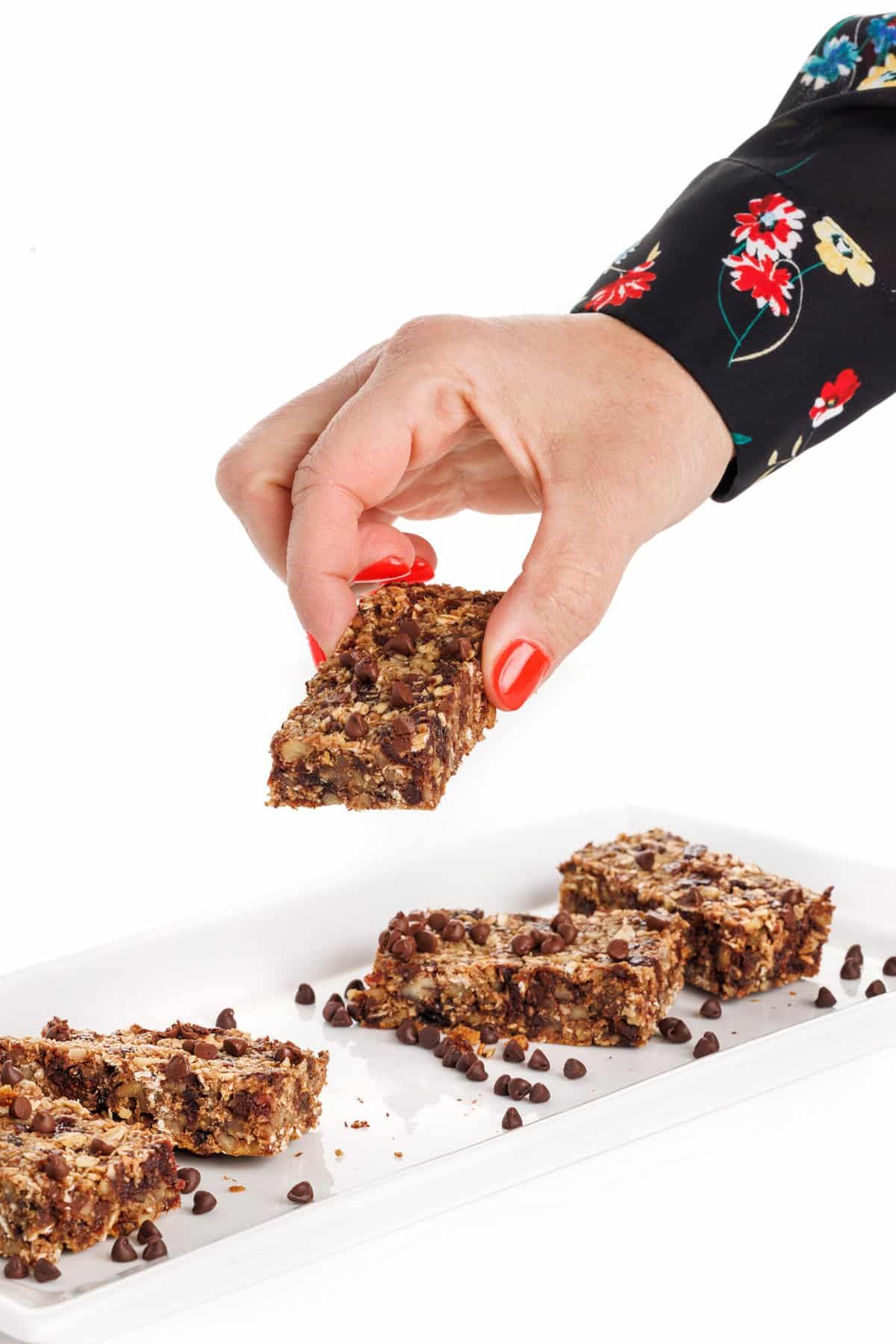 Hand grabbing a seedy oat and flax granola bar off a white plate.