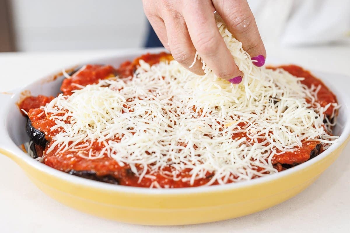 Sprinkling grated parmesan cheese over the top of eggplant.