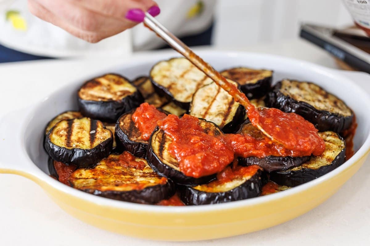 Grilled eggplant in baking dish topped with tomato sauce.