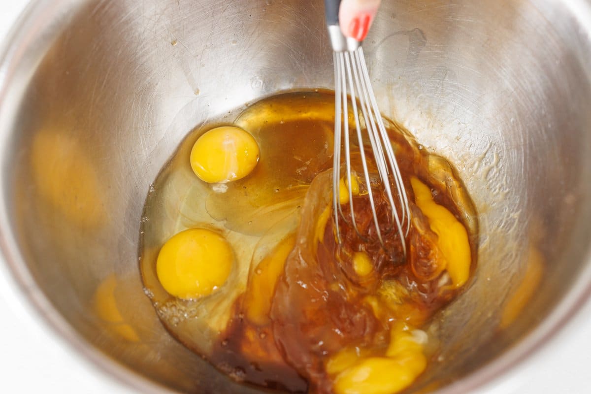Whisking eggs with honey and vanilla in a large metal bowl.