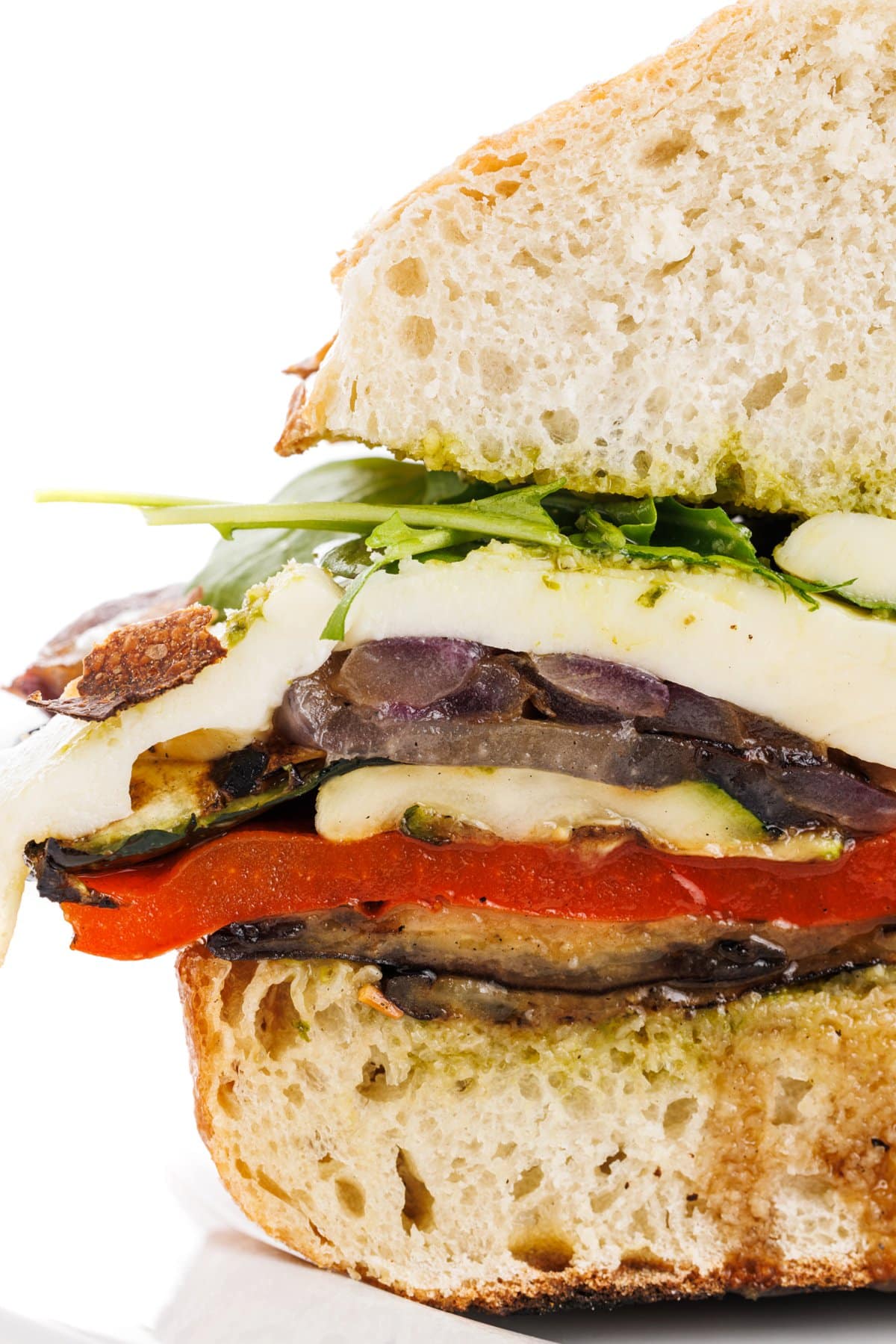 Grilled vegetable sandwich with pesto and mozzarella cut in half.