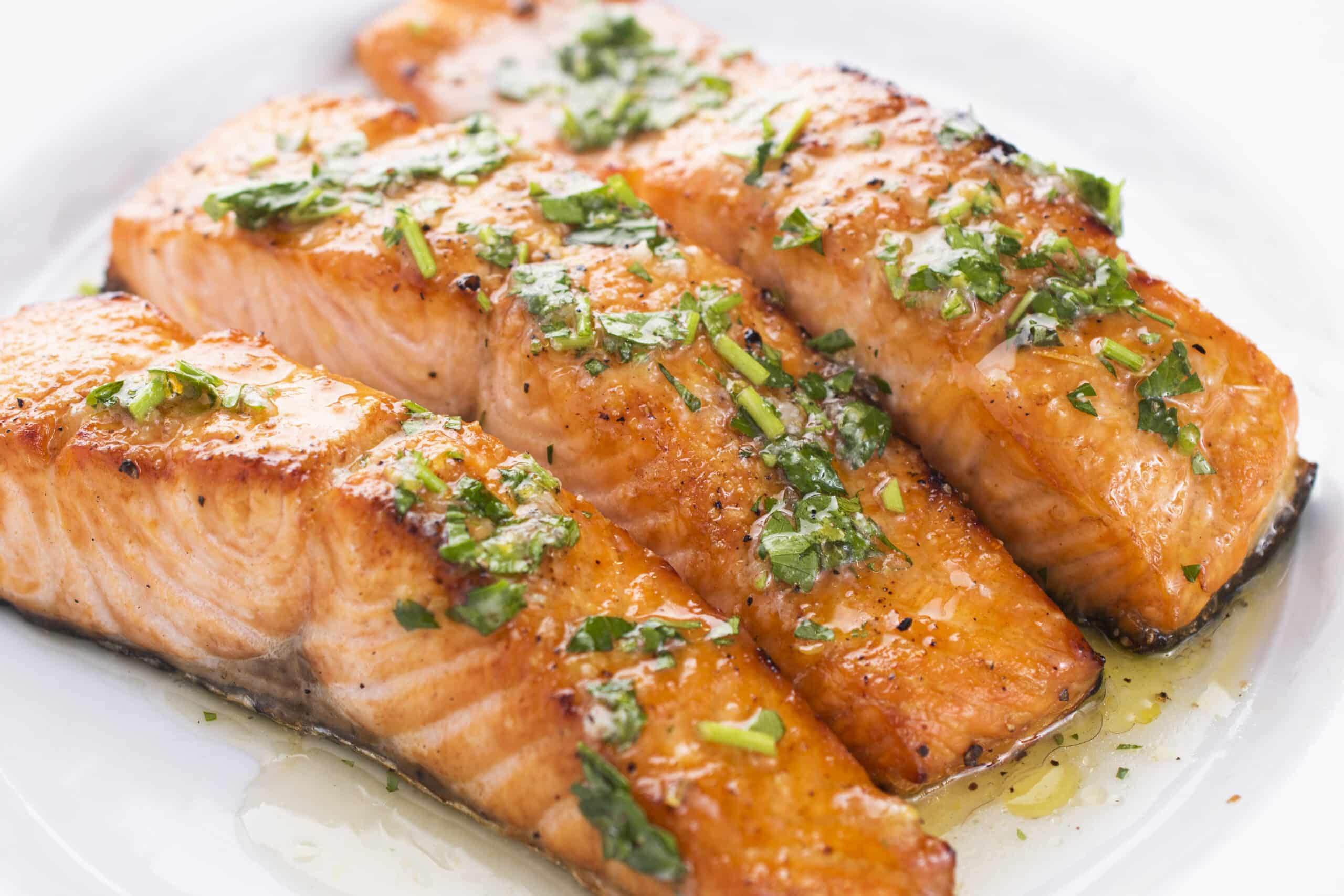 Grilled salmon with garlic and lemon on a plate topped with fresh herbs.