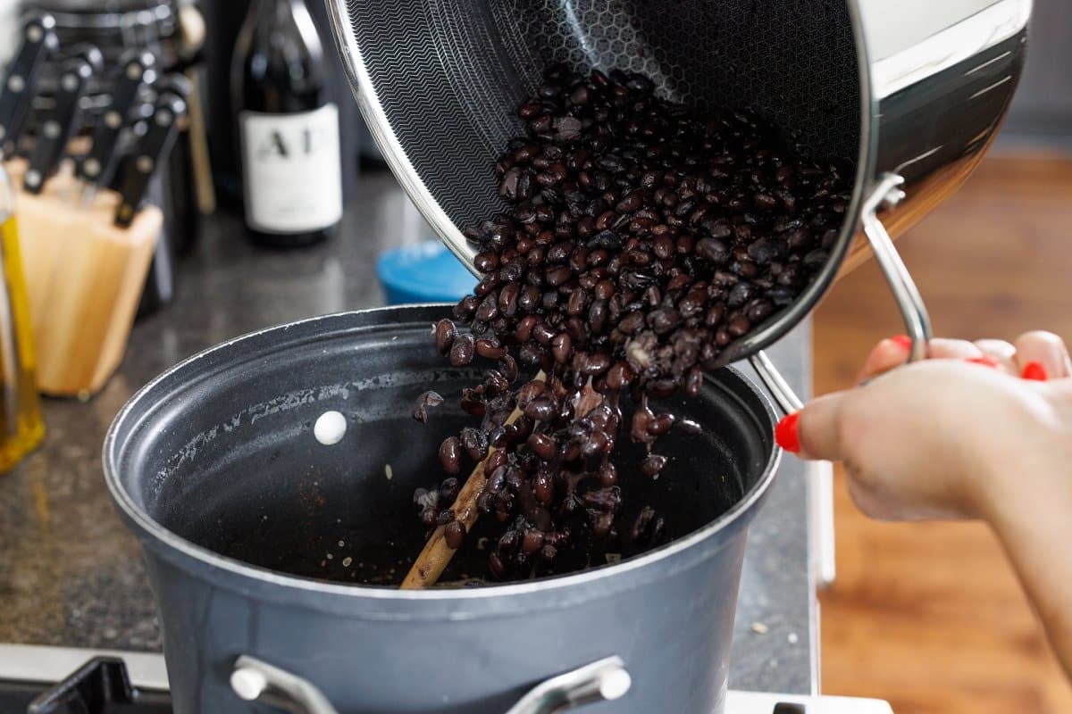Adding cooked black beans to the pot of rice.