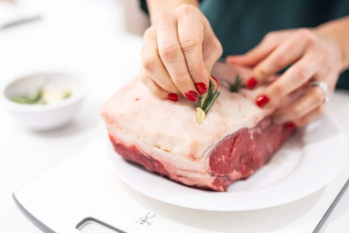 Shoving rosemary sprigs into slits in beef roast.