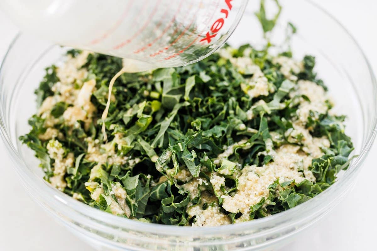 Pouring dressing over kale caesar salad.