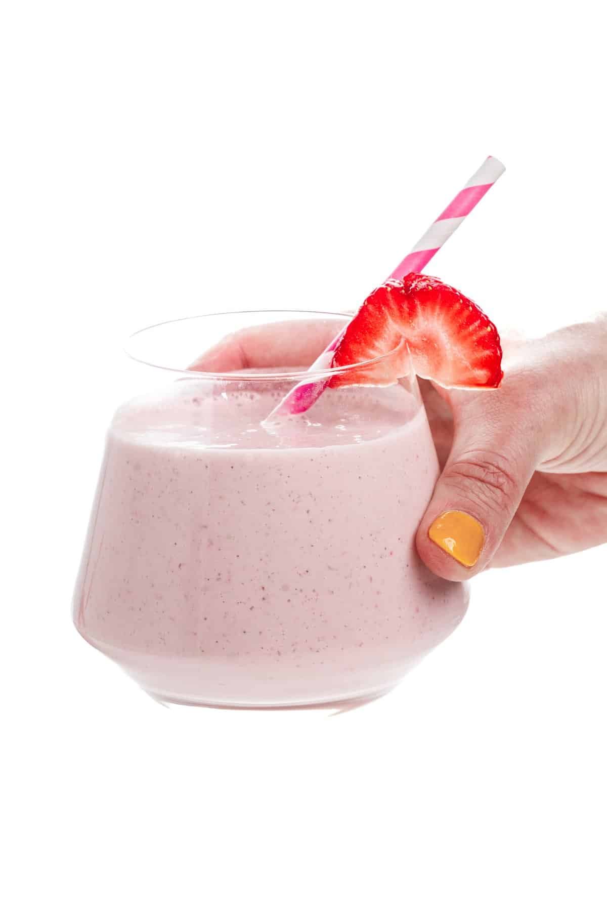 Hand holding a strawberry protein smoothie.