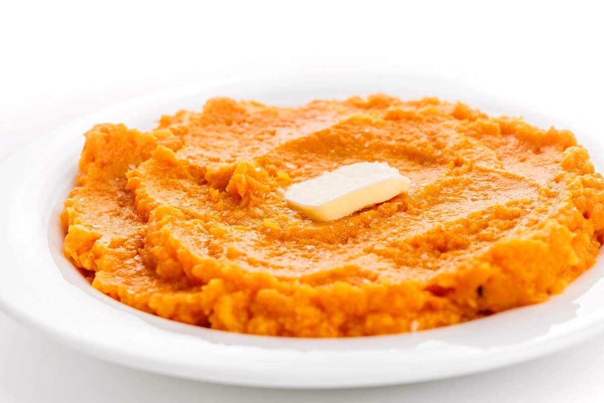 Mashed butternut squash and sweet potatoes spread across a plate with a square of butter in the center.