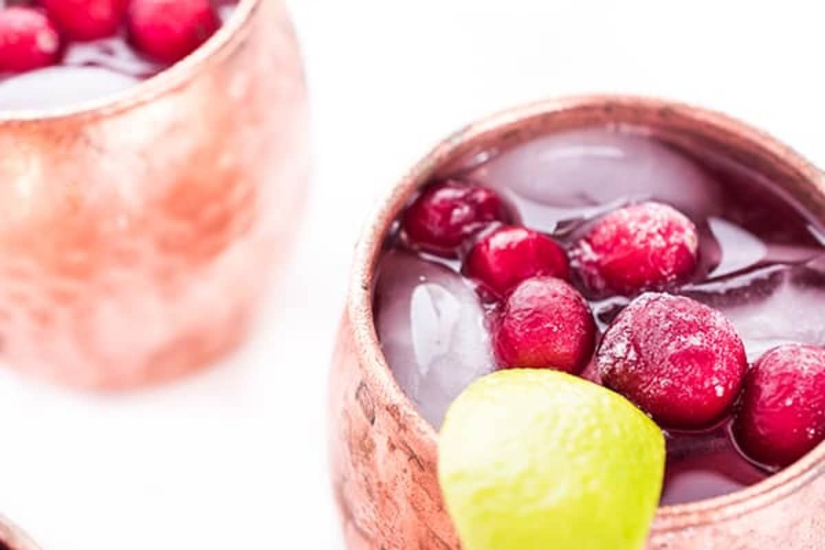 Close up to an easy Cranberry Moscow Mule in a copper mug, with fresh cranberries and a lime wedge as garnish.