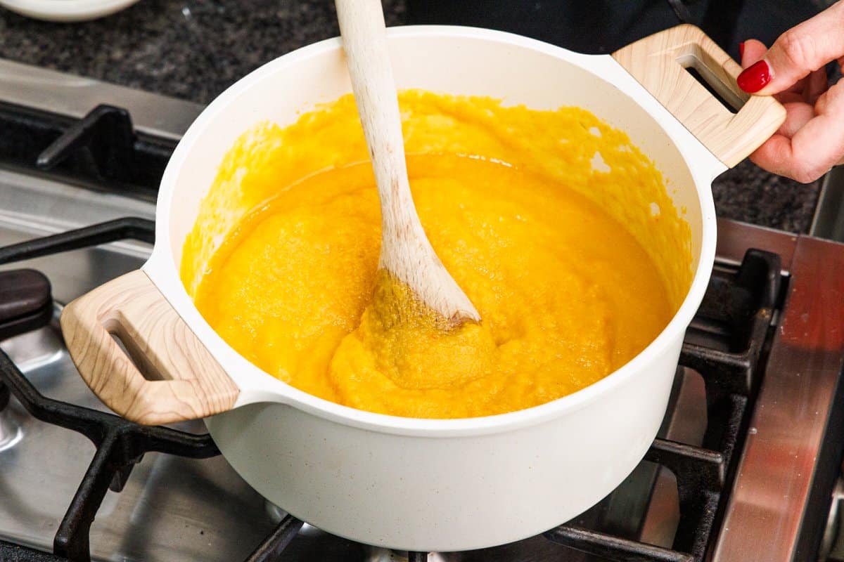 Wooden spoon stirring root vegetable soup on the stove.
