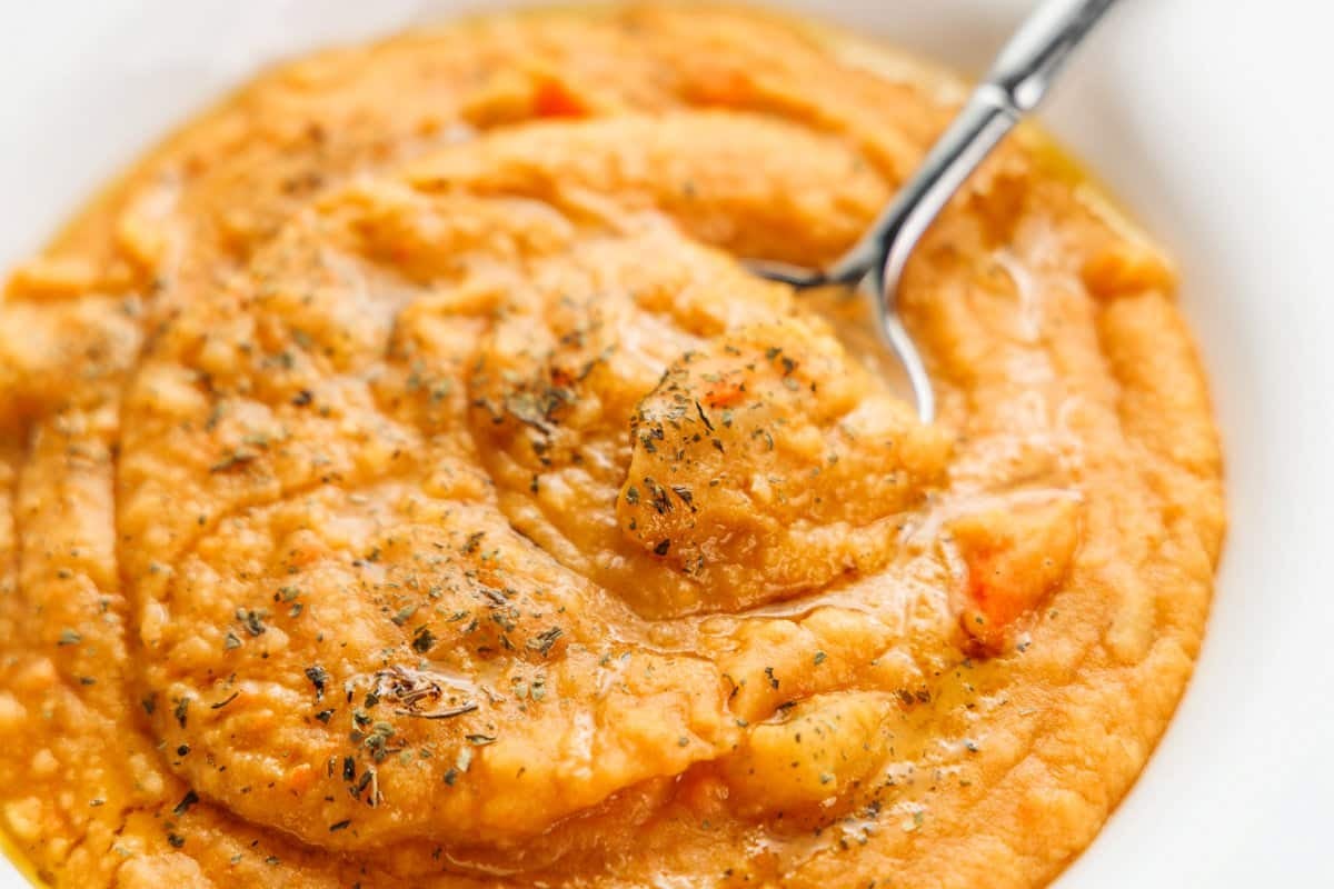 A spoon sitting in red lentil soup garnished with mint.