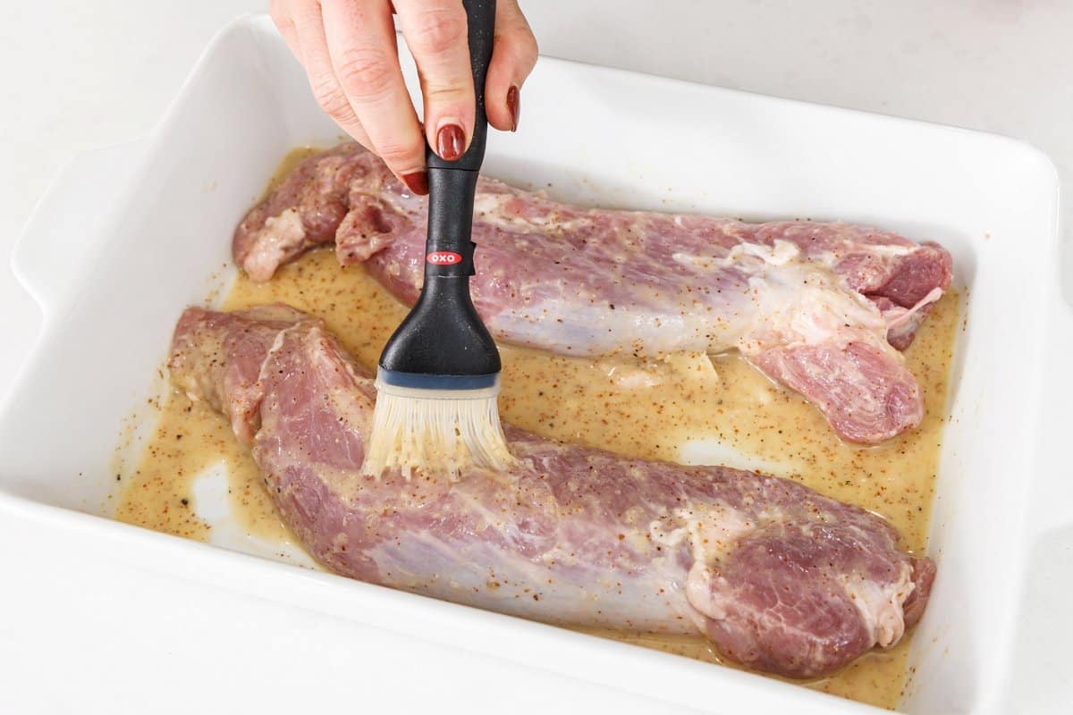 Using a brush to apply mustard glaze to pork tenderloin.