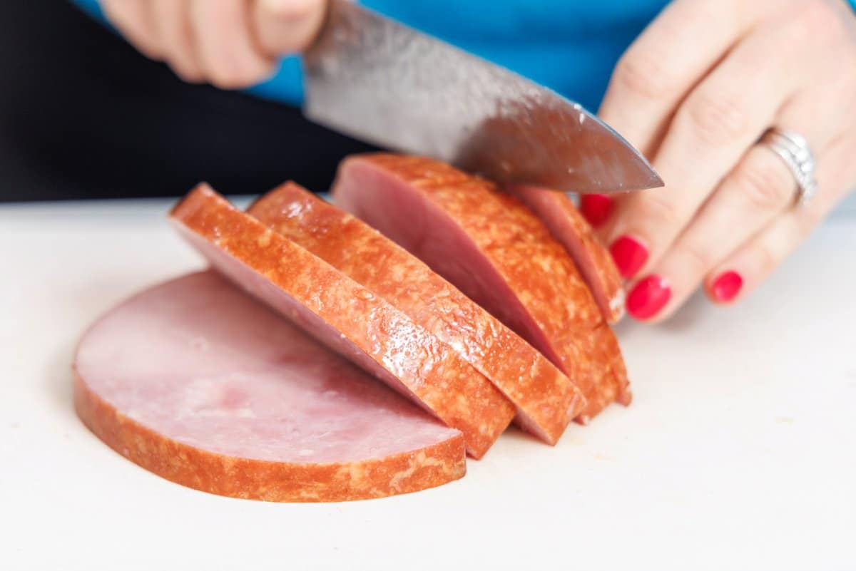 Cutting precooked ham into cubes with a sharp knife.