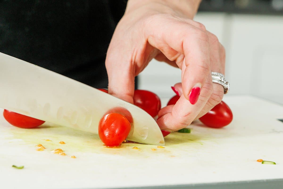 Cutting grape tomatoes in half with a sharp knife.