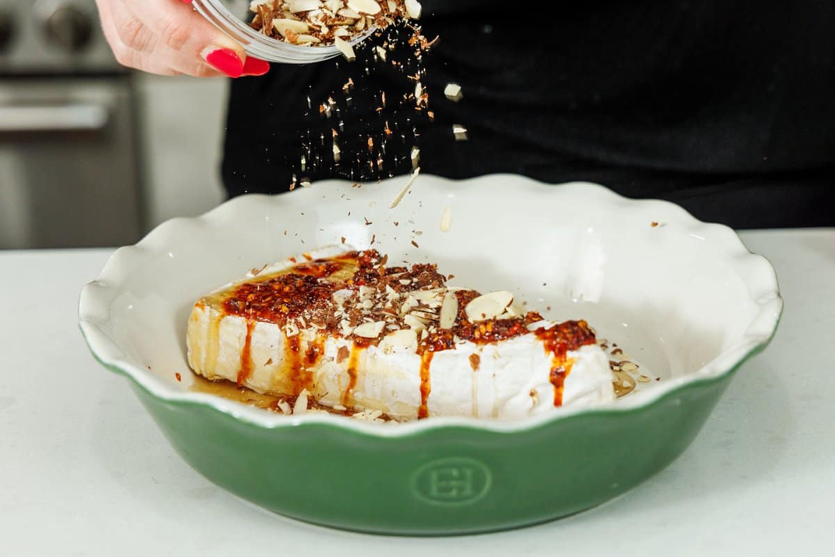 Topping hot honey brie with slivered almonds in a baking dish.