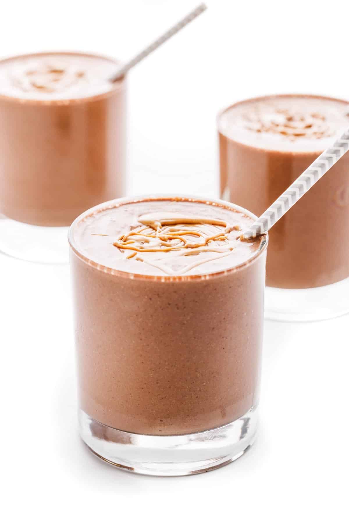Chocolate peanut butter protein smoothies in short glasses with straws in each glass.