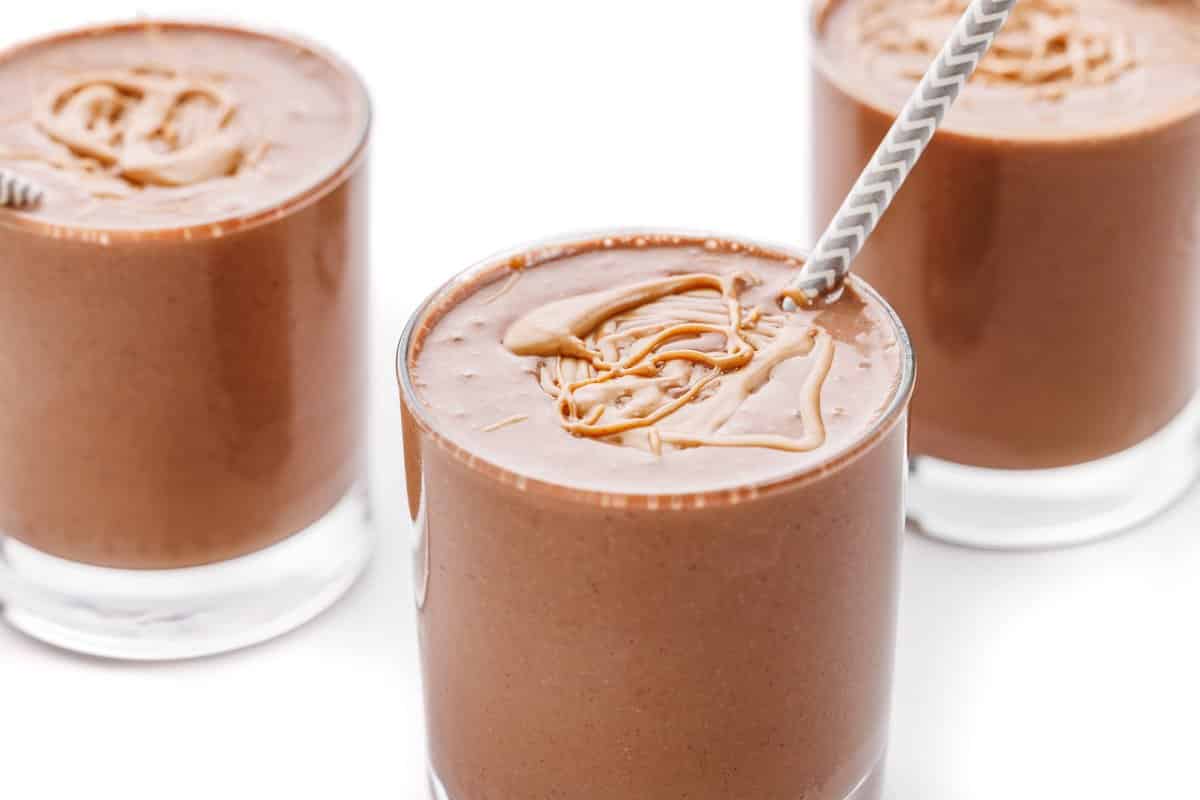Three glasses in a row with chocolate peanut butter protein smoothie in each.