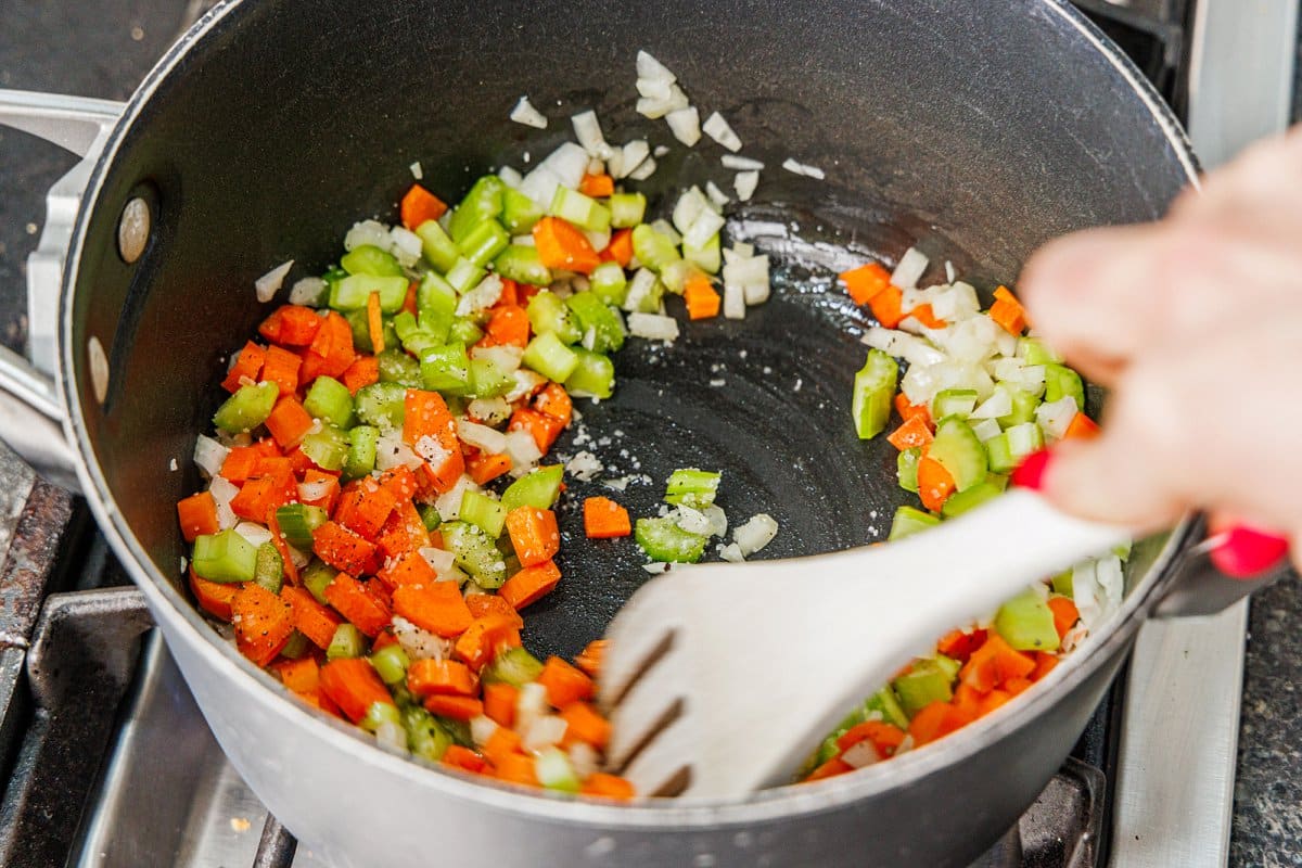 Sautéing diced onion, celery, and carrot in the bottom of a large pot.