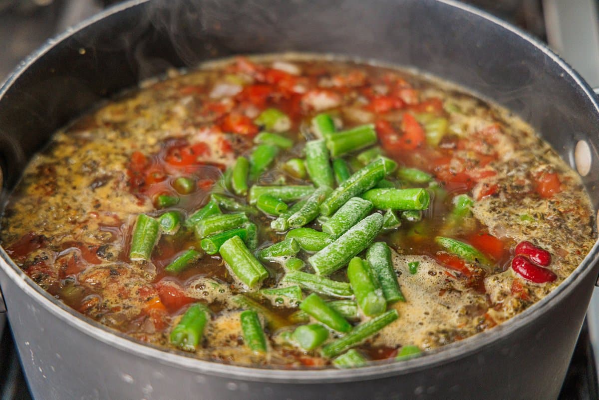 Frozen green beans added to a large pot of minestrone soup.