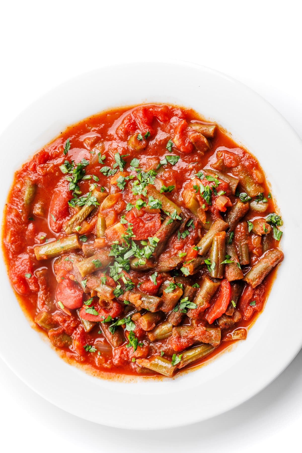 Lebanese green beans with tomatoes garnished with fresh parsley in a white bowl.