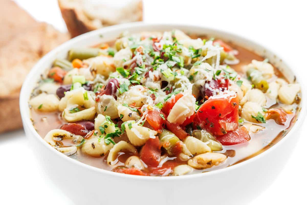 Minestrone soup in a bowl with crust bread in the background.