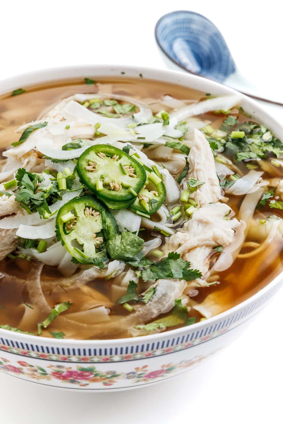 Slow cooker pho-inspired chicken soup in a bowl with a Chinese soup spoon in the background.