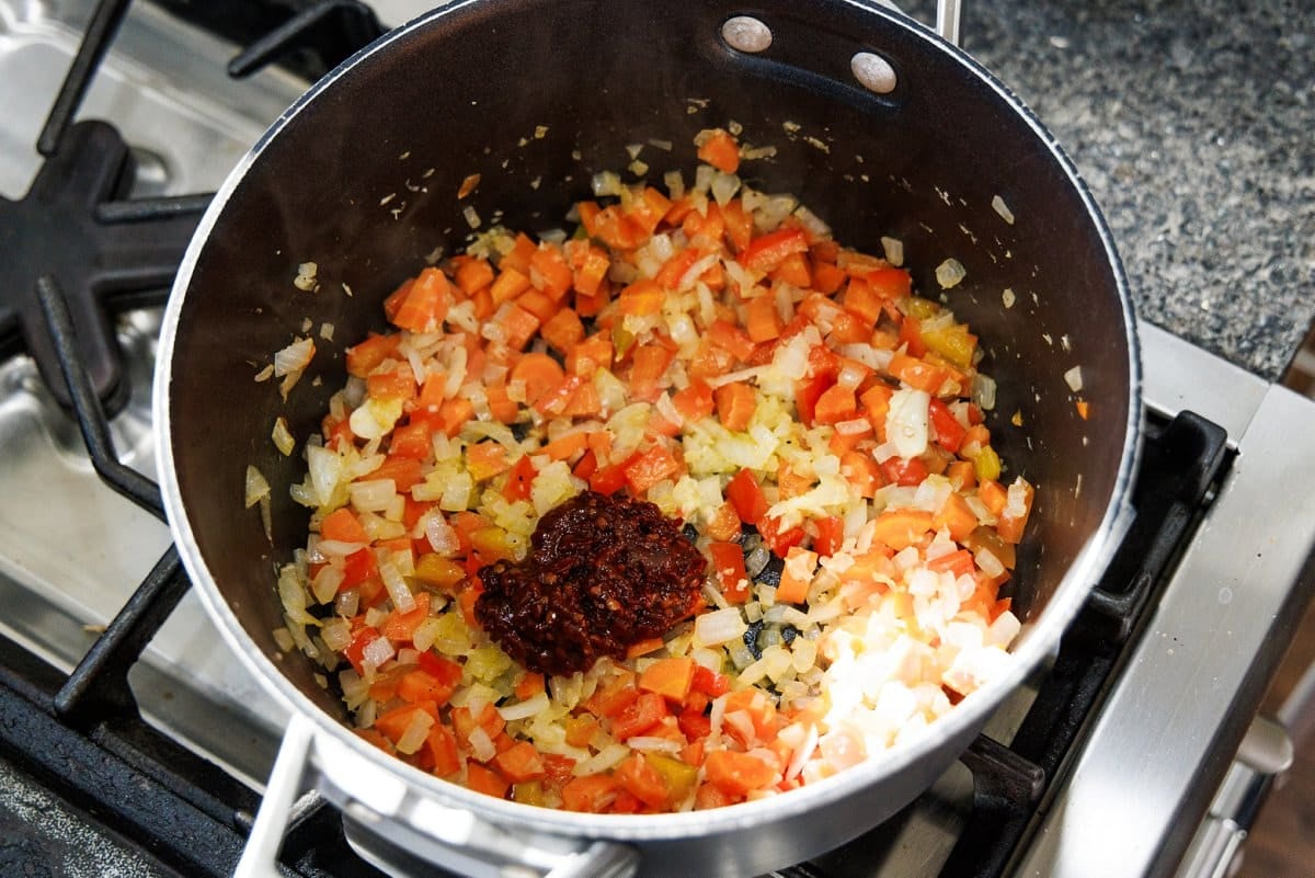 Adding chopped chipotle peppers in adobo sauce to veggies in soup pot.