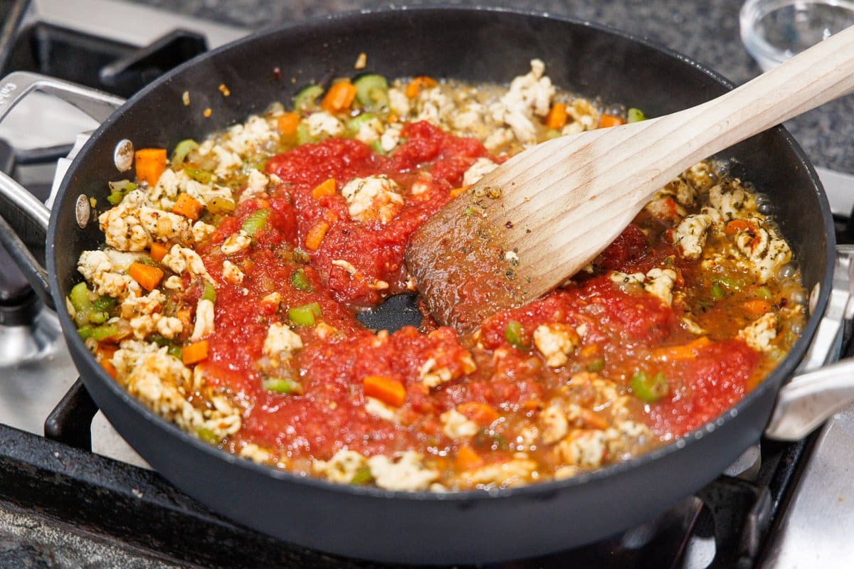 Stirring in crushed tomatoes to cooked veggies and ground trukey.