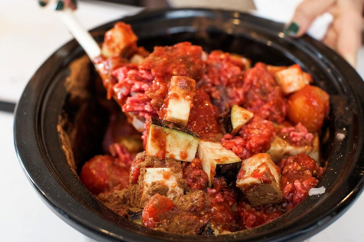 Stirring eggplant, beef, and crushed tomatoes with Lebanese spice blend in a slow cooker.