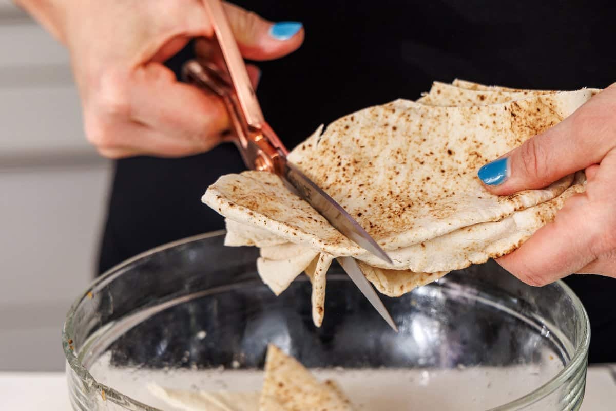 Cutting pita bread into triangles with scissors.