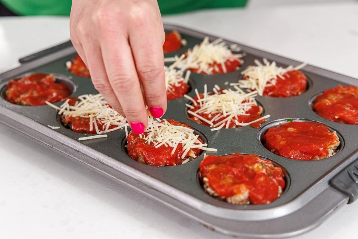 Topping meatloaf muffins with marinara sauce and cheese.