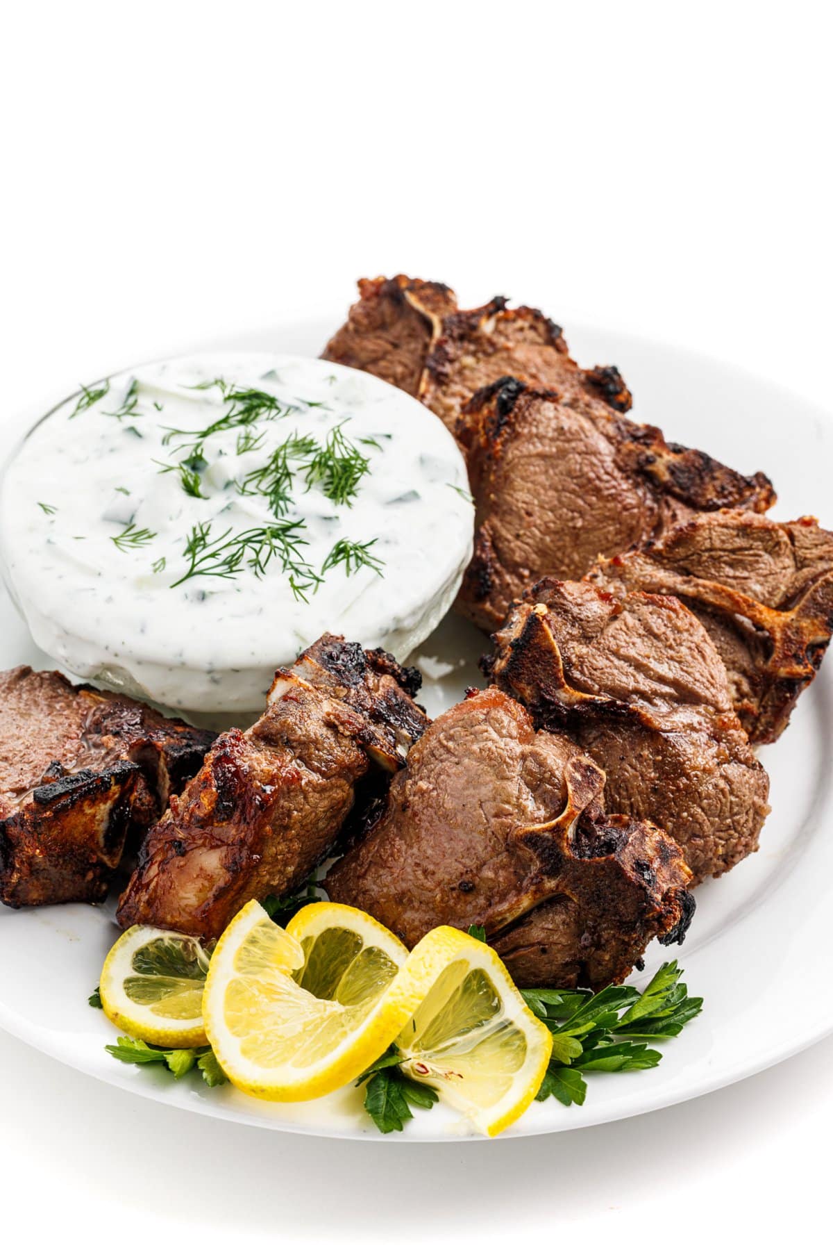 Greek lamb chops with tzatziki sauce  in a small bowl next to them.