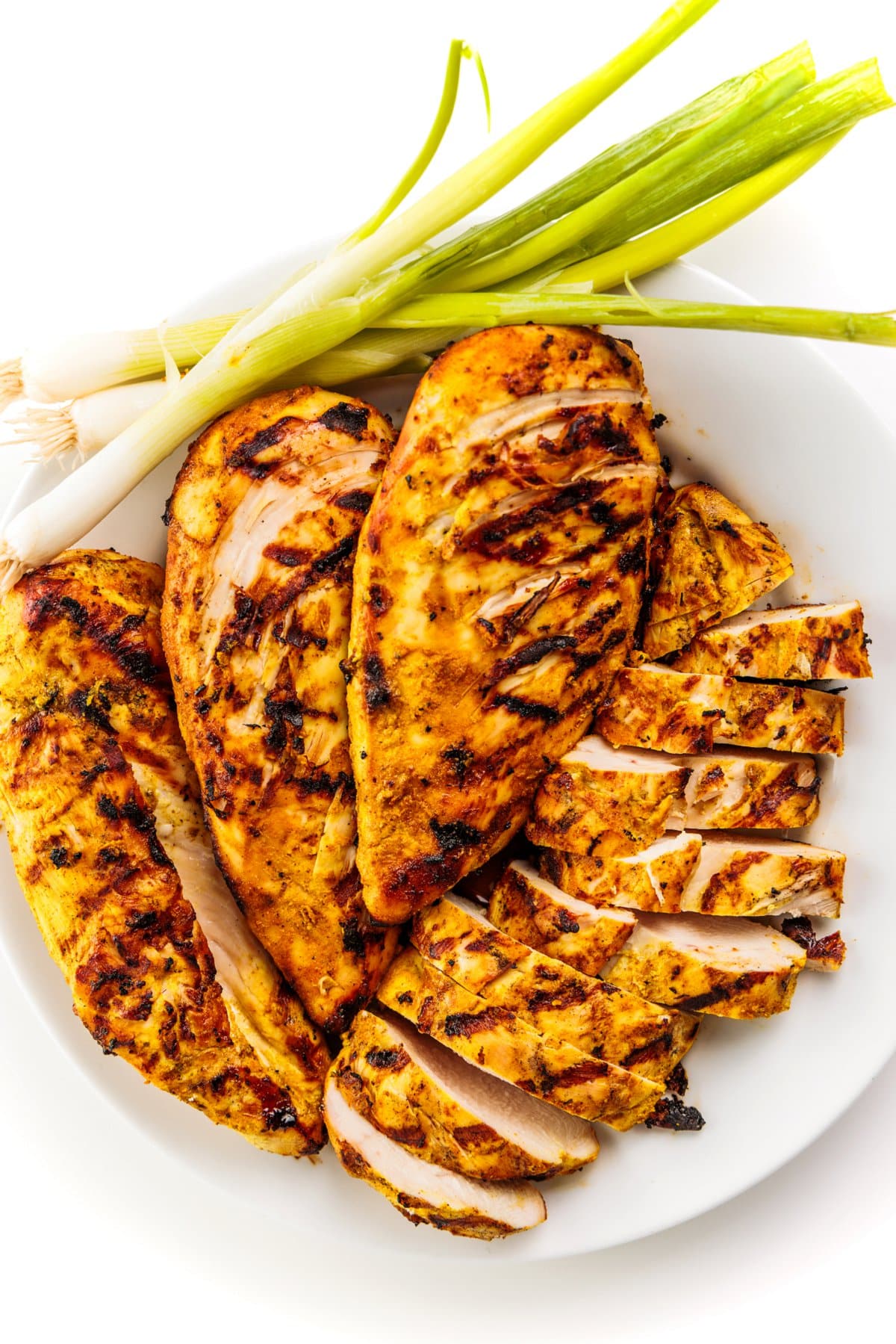 Indian spiced grilled chicken on a plate with green onions.