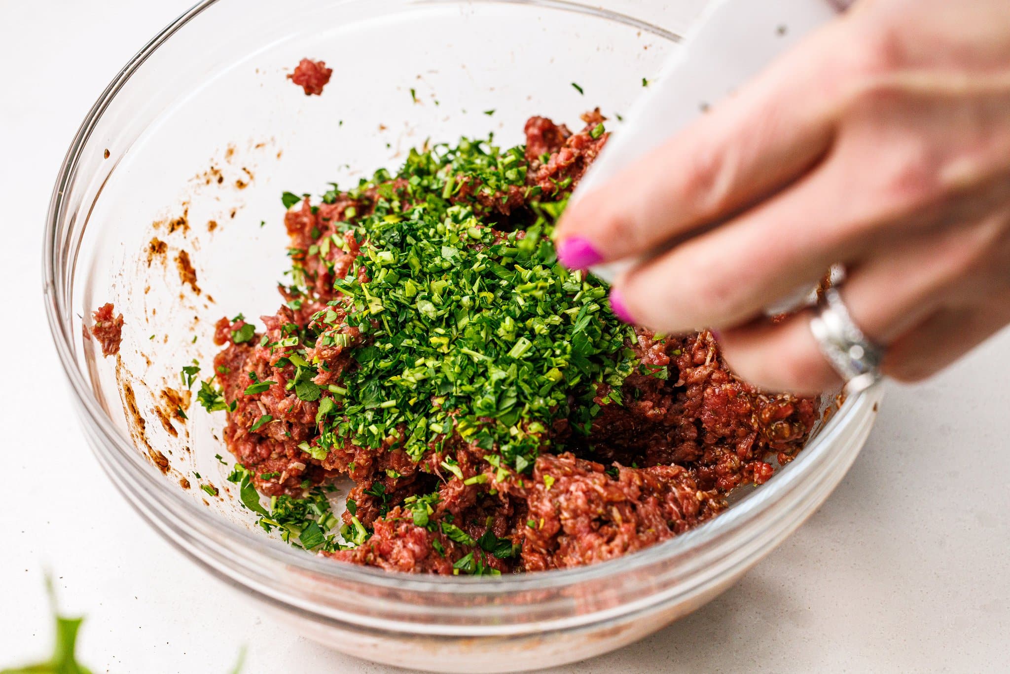 Adding freshly chopped parsley to bowl of meat.