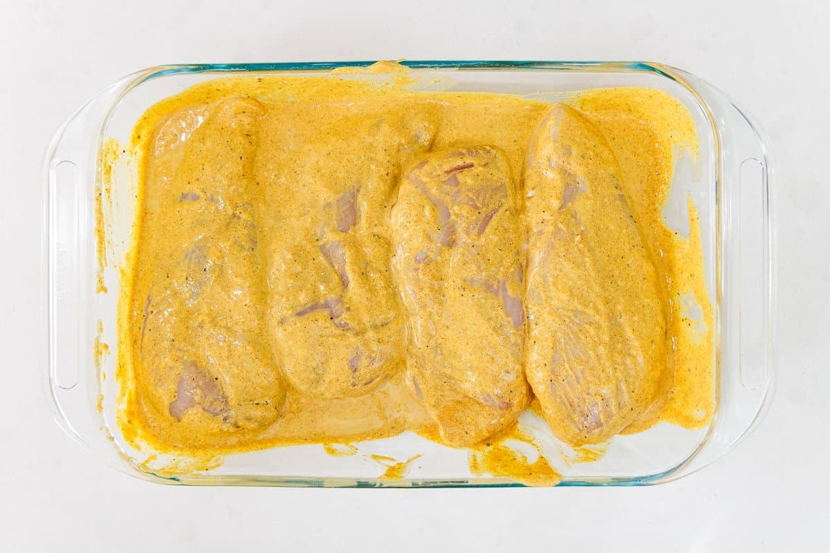 Chicken in a glass baking dish covered in Indian spiced marinade.