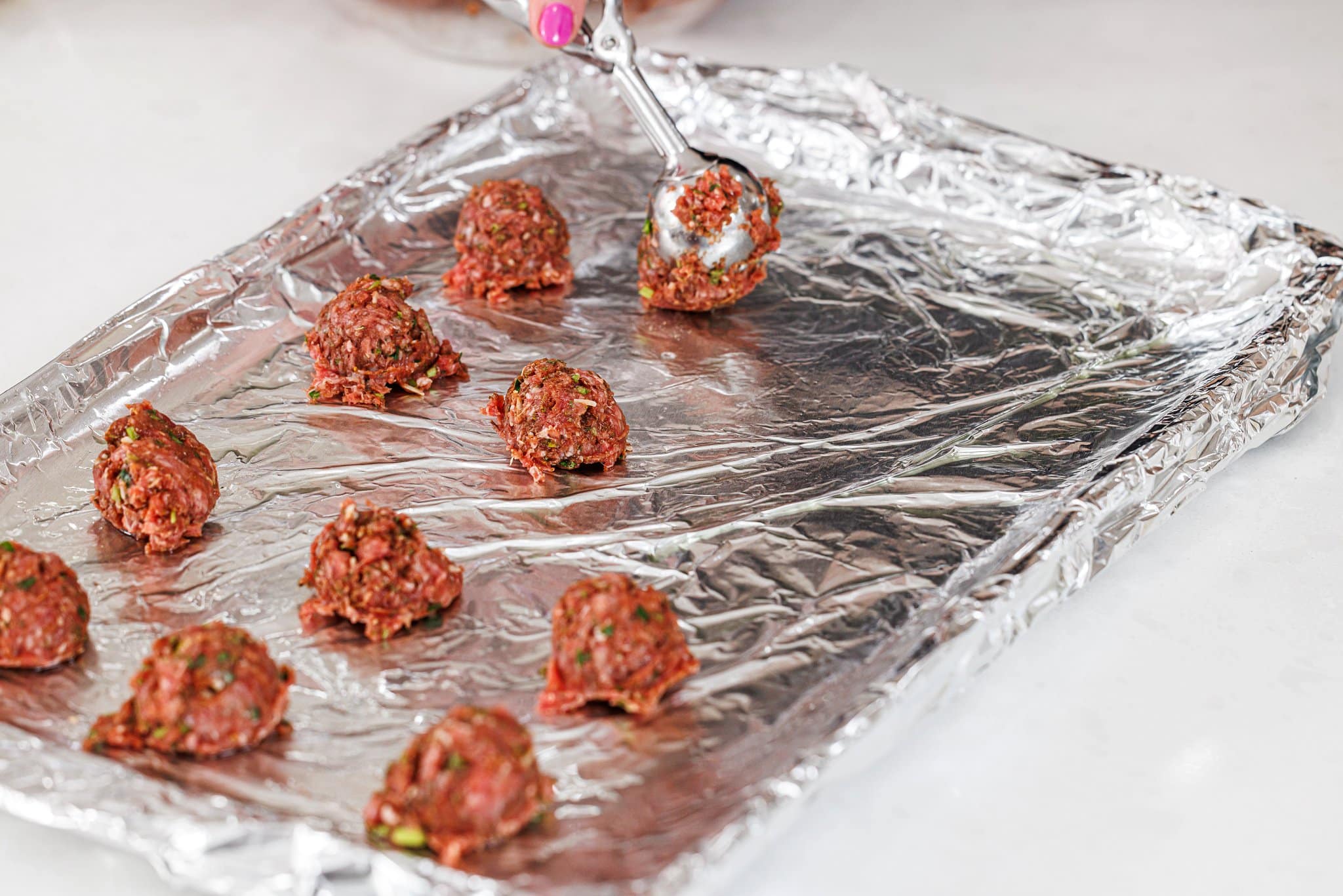Putting uncooked meatballs on a prepared baking sheet.