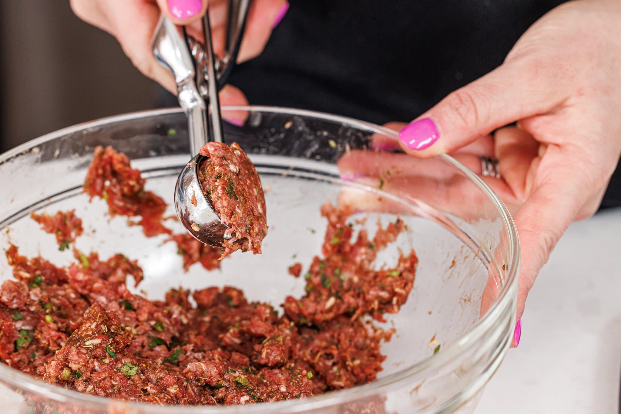 Using a cookie scoop to portion meat mixture from bowl.