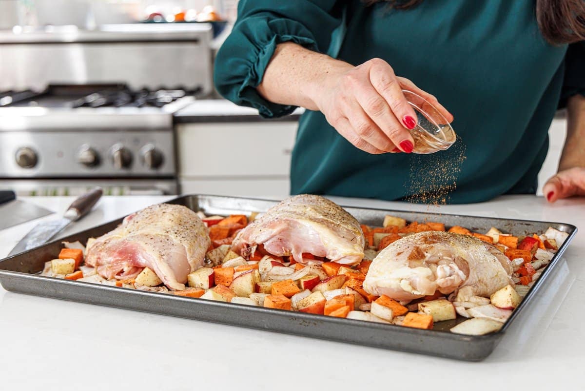 Seasoning chicken breast on sheet pan with veggies.