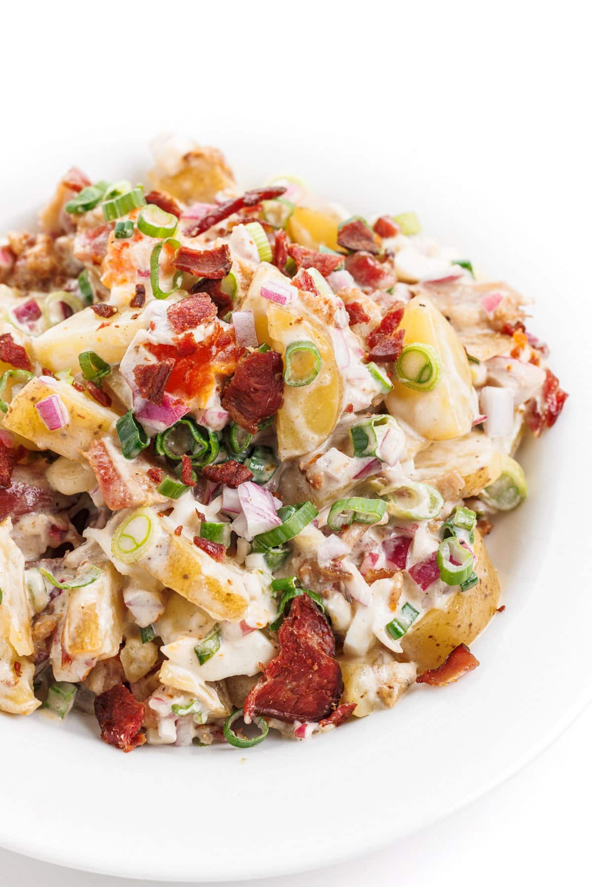Potato salad with bacon and eggs in a bowl topped with fresh scallions.