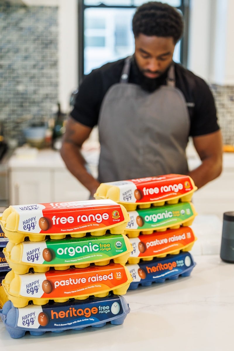Chef Trimell standing behind a counter with 6 dozen cartons of Happy Egg eggs.