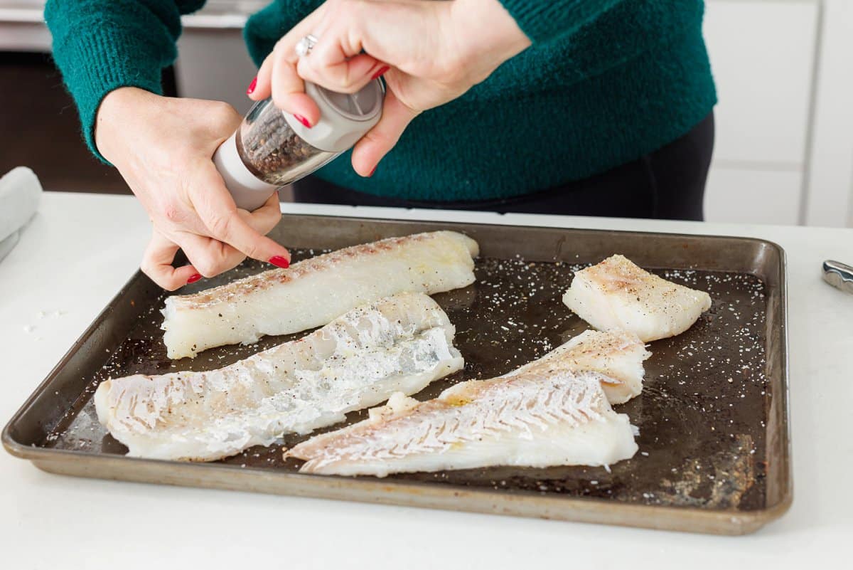 Seasoning white fish with a pepper grinder.