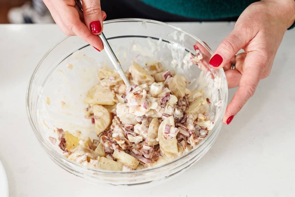 Stirring together potato salad in large glass bowl.