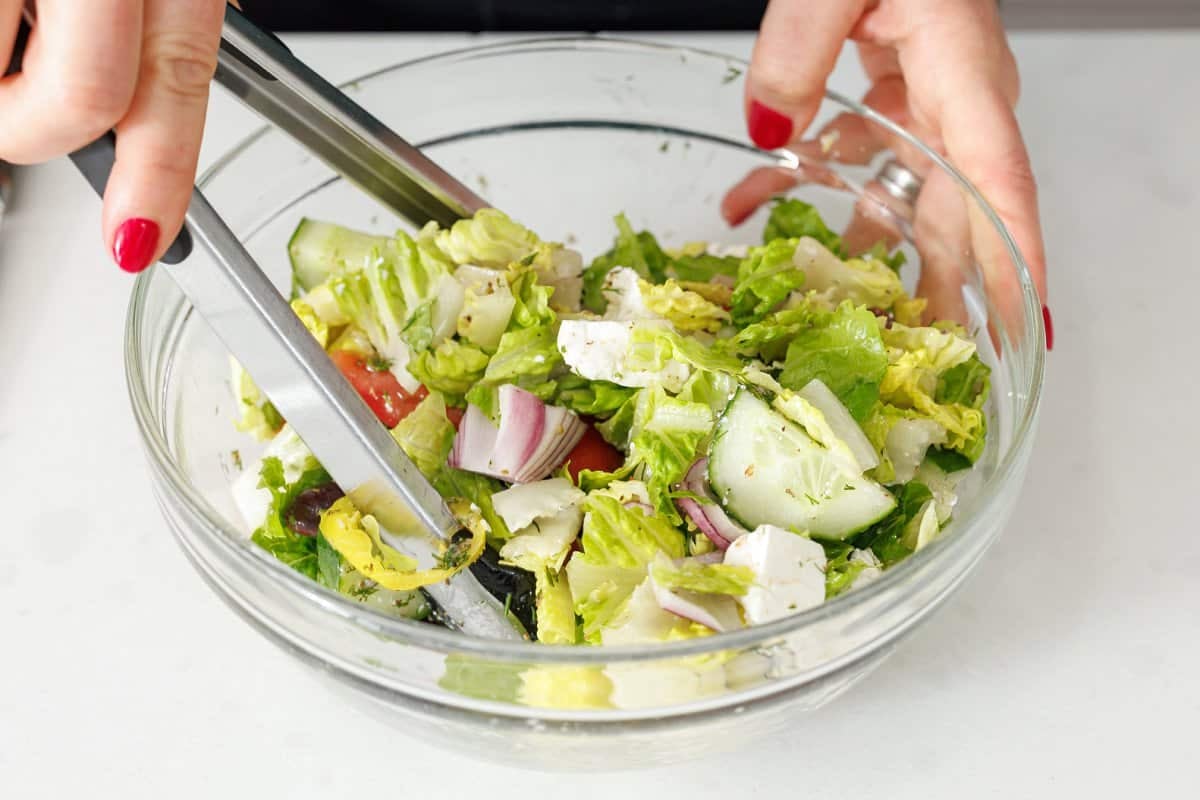 Tossing together a Greek salad with metal tongs.