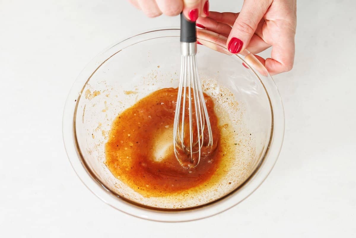 Whisking together honey lime vinaigrette in glass bowl.