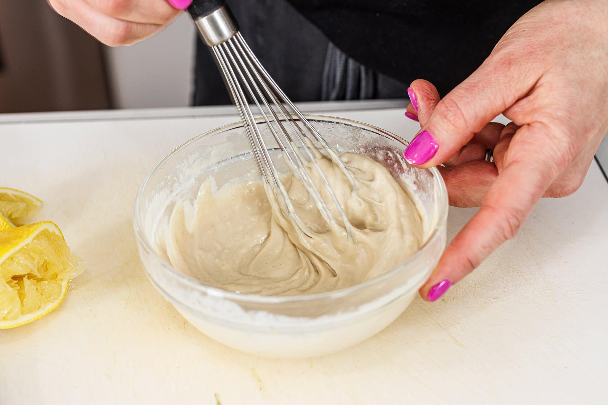 Whisking tahini dipping sauce in glass bowl.