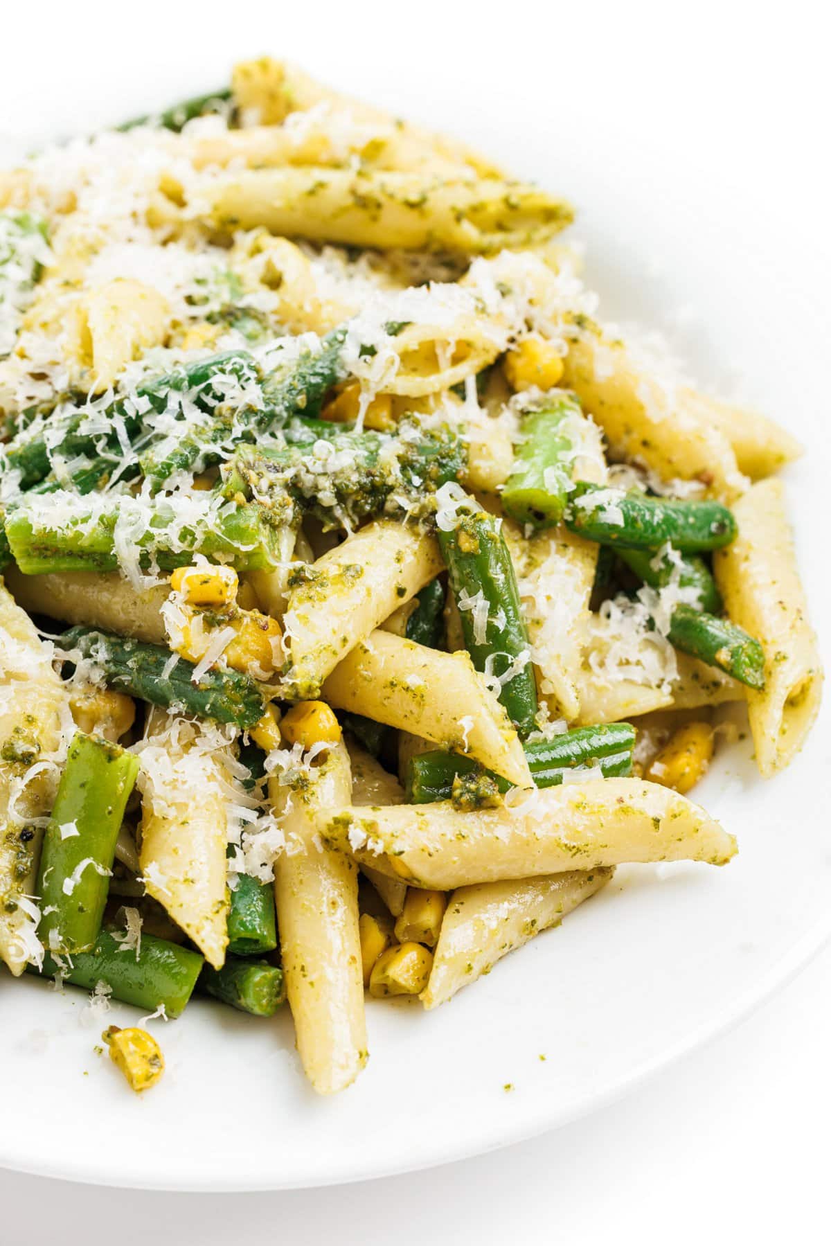 Pesto pasta salad with green beans and corn topped with shredded parmesan cheese.