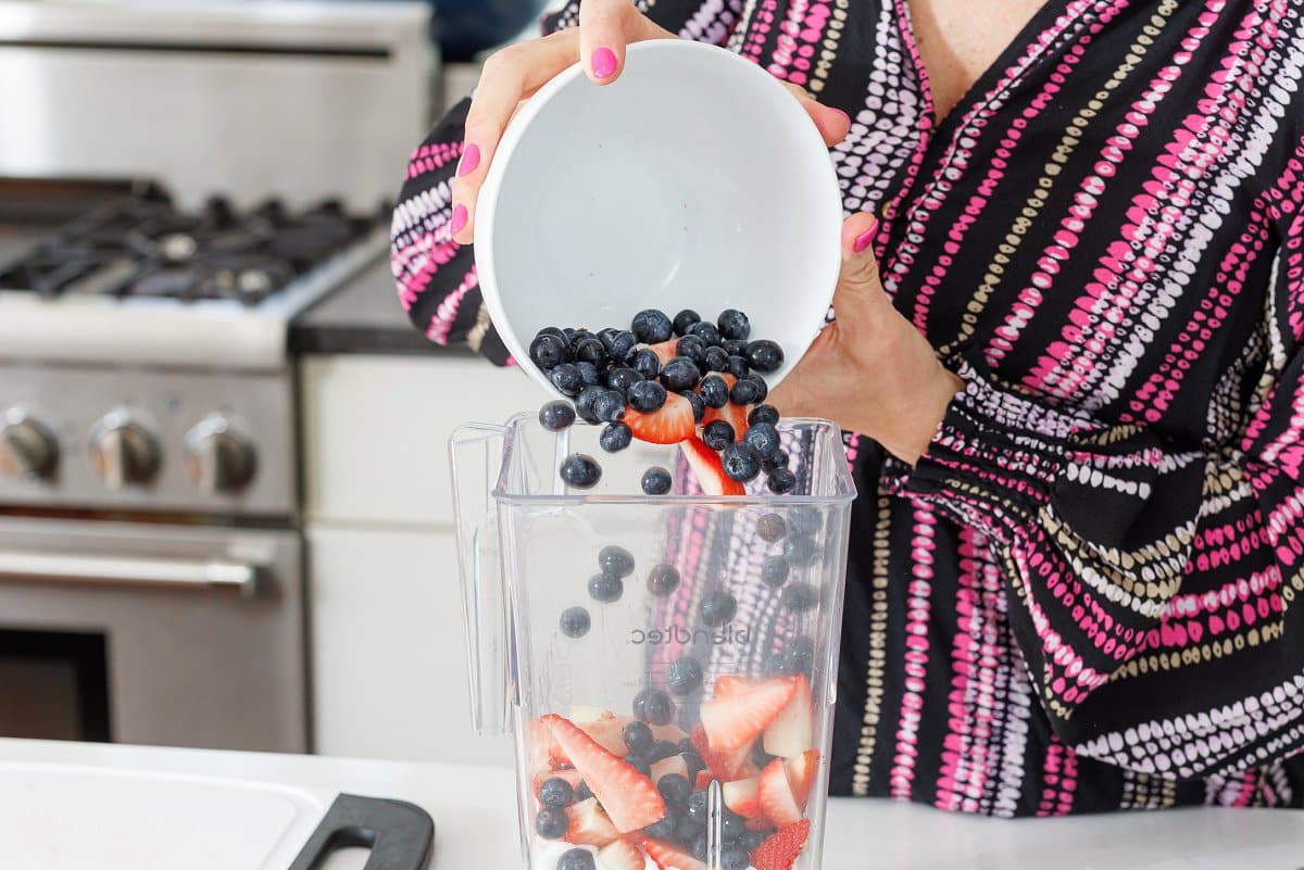 Adding fresh blueberries and strawberries to a blender.
