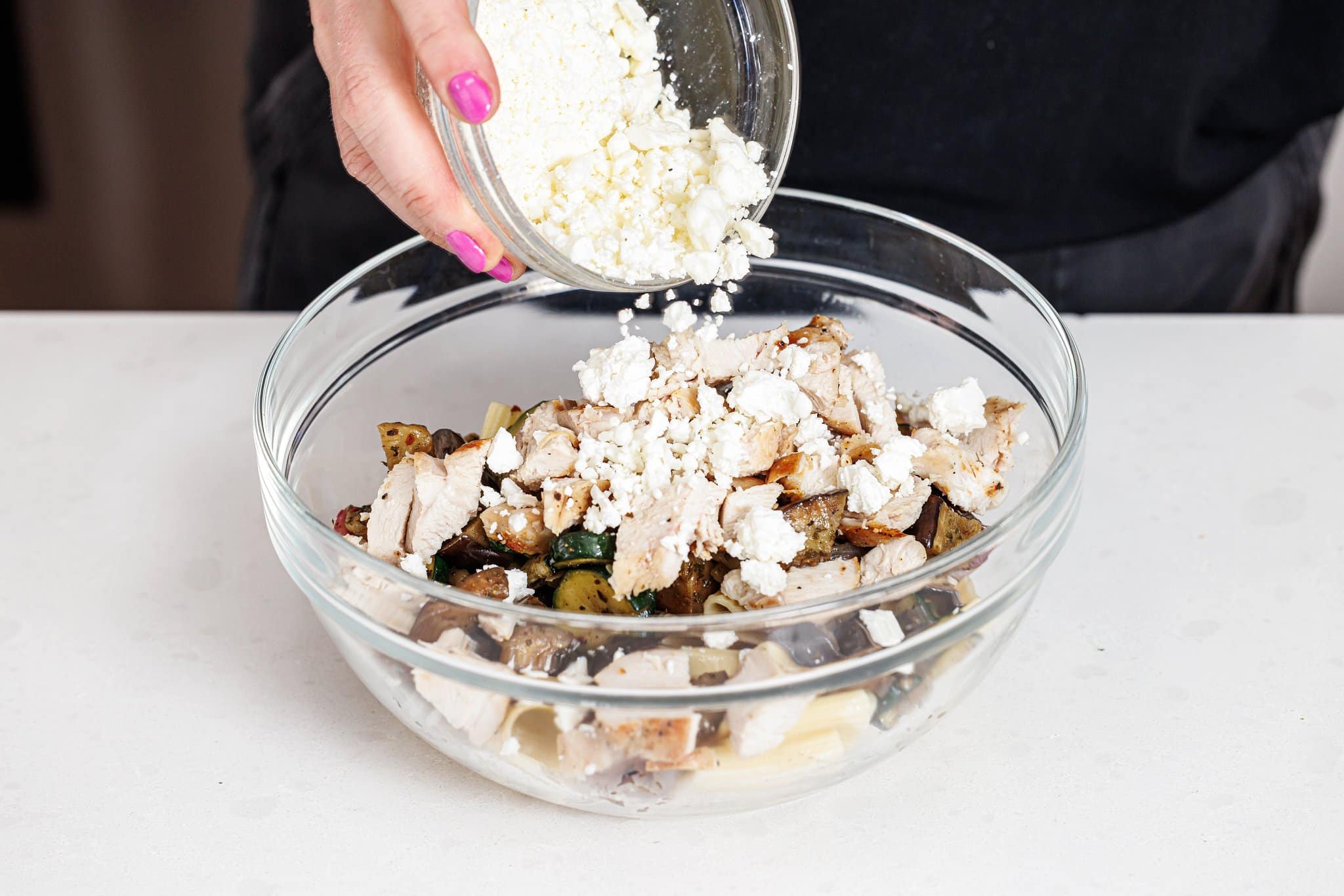 Adding crumbled feta cheese to pasta salad.