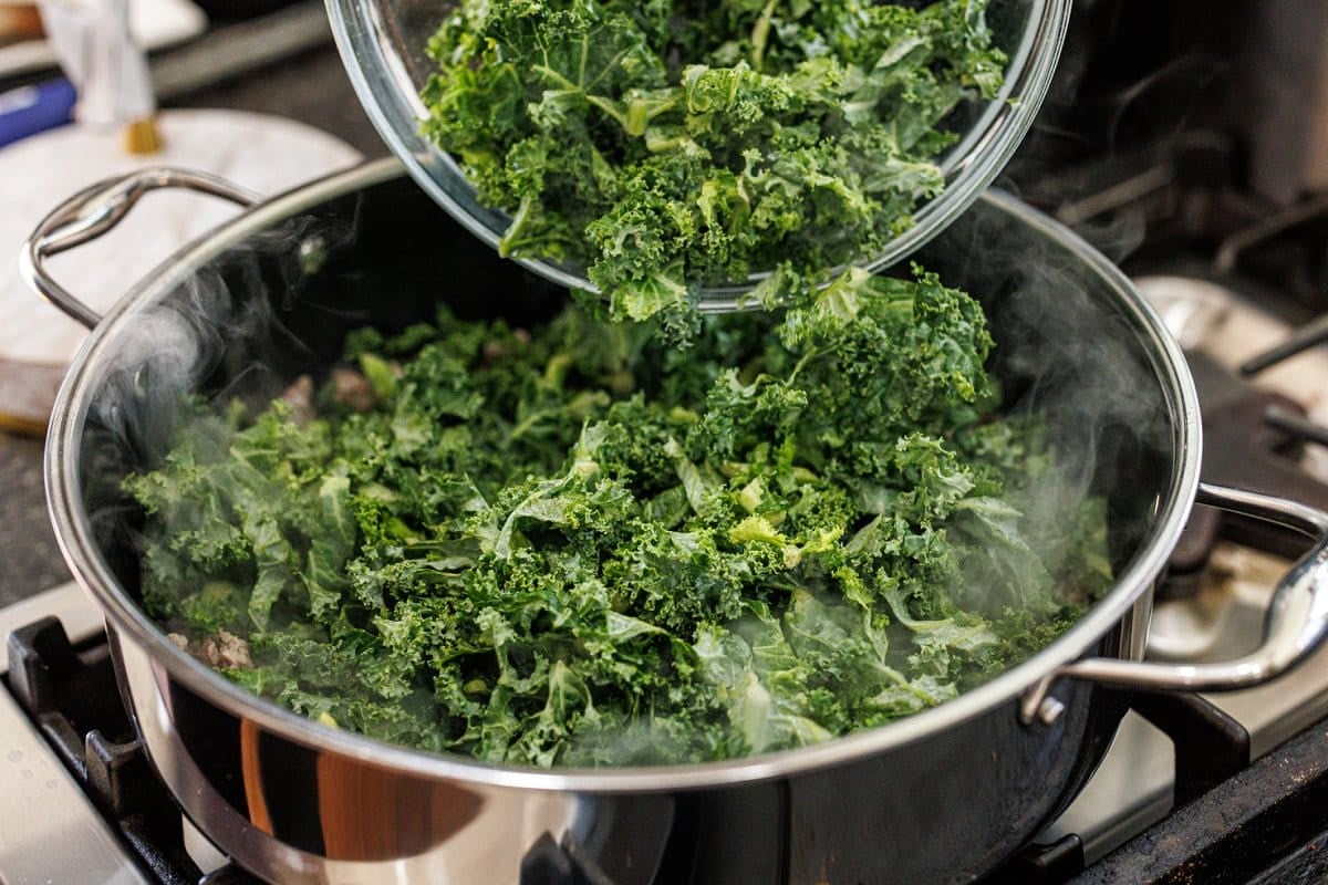 Adding chopped kale to skillet.