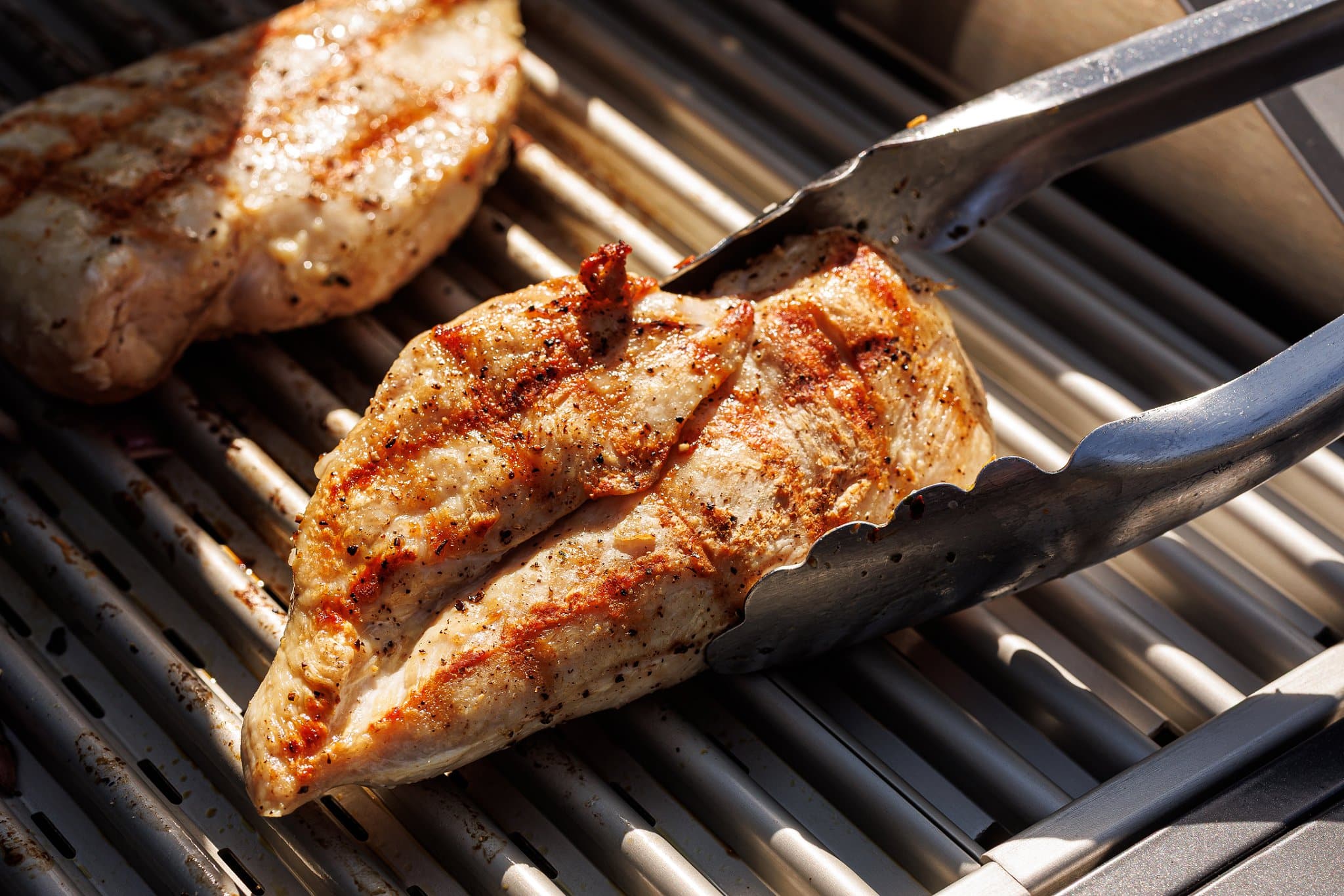 Chicken breasts grilling on outdoor grill.